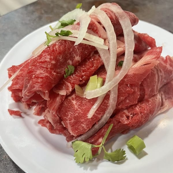 Thinly sliced raw beef, onions, and herbs on a white plate, ready for Vietnamese pho.