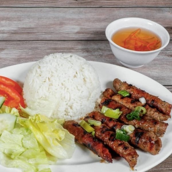 Boba Pho U's Vietnamese grilled pork, rice, salad, and a side of broth on a white plate.