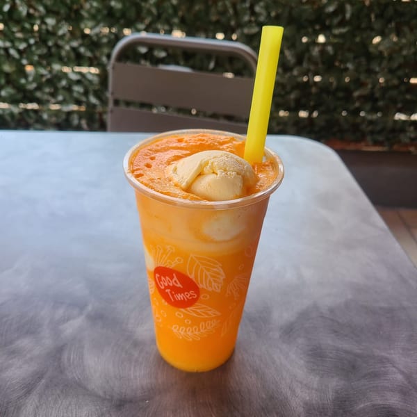 Orange boba drink with a scoop of ice cream and a yellow straw on a metal table.