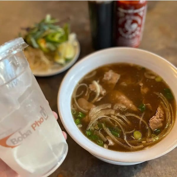 A bowl of Boba Pho U pho with a side of fresh herbs and a drink.