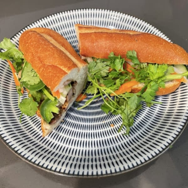 A Vietnamese banh mi sandwich, cut in half, filled with meat, cilantro, and vegetables on a patterned plate.