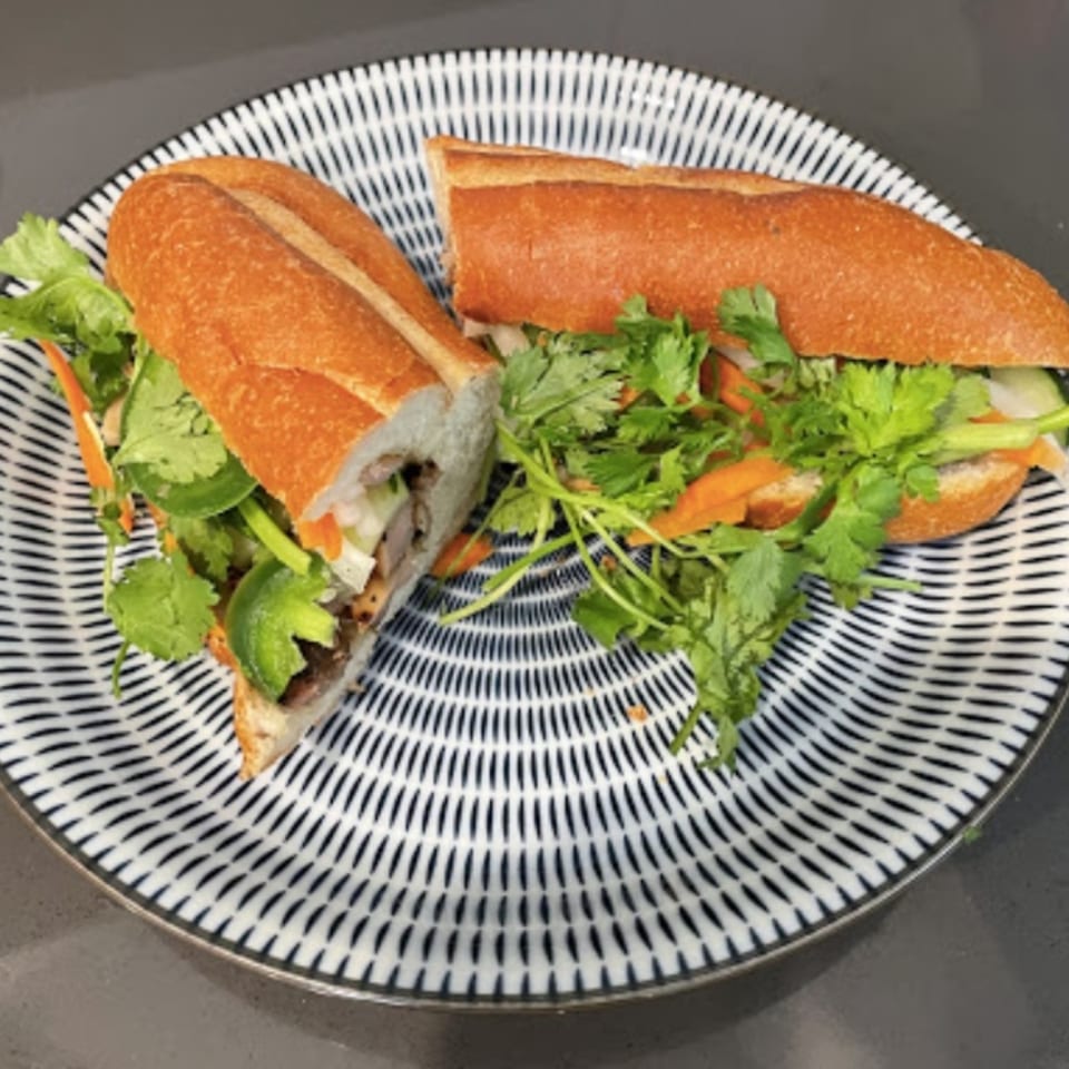 A Vietnamese banh mi sandwich, cut in half, filled with meat, cilantro, and vegetables on a patterned plate.