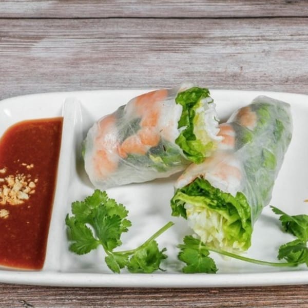Two fresh Vietnamese spring rolls with shrimp and lettuce, served with peanut sauce and cilantro.